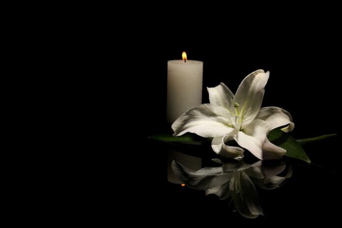White lily and candle on black background for funeral or obituary, obituaries