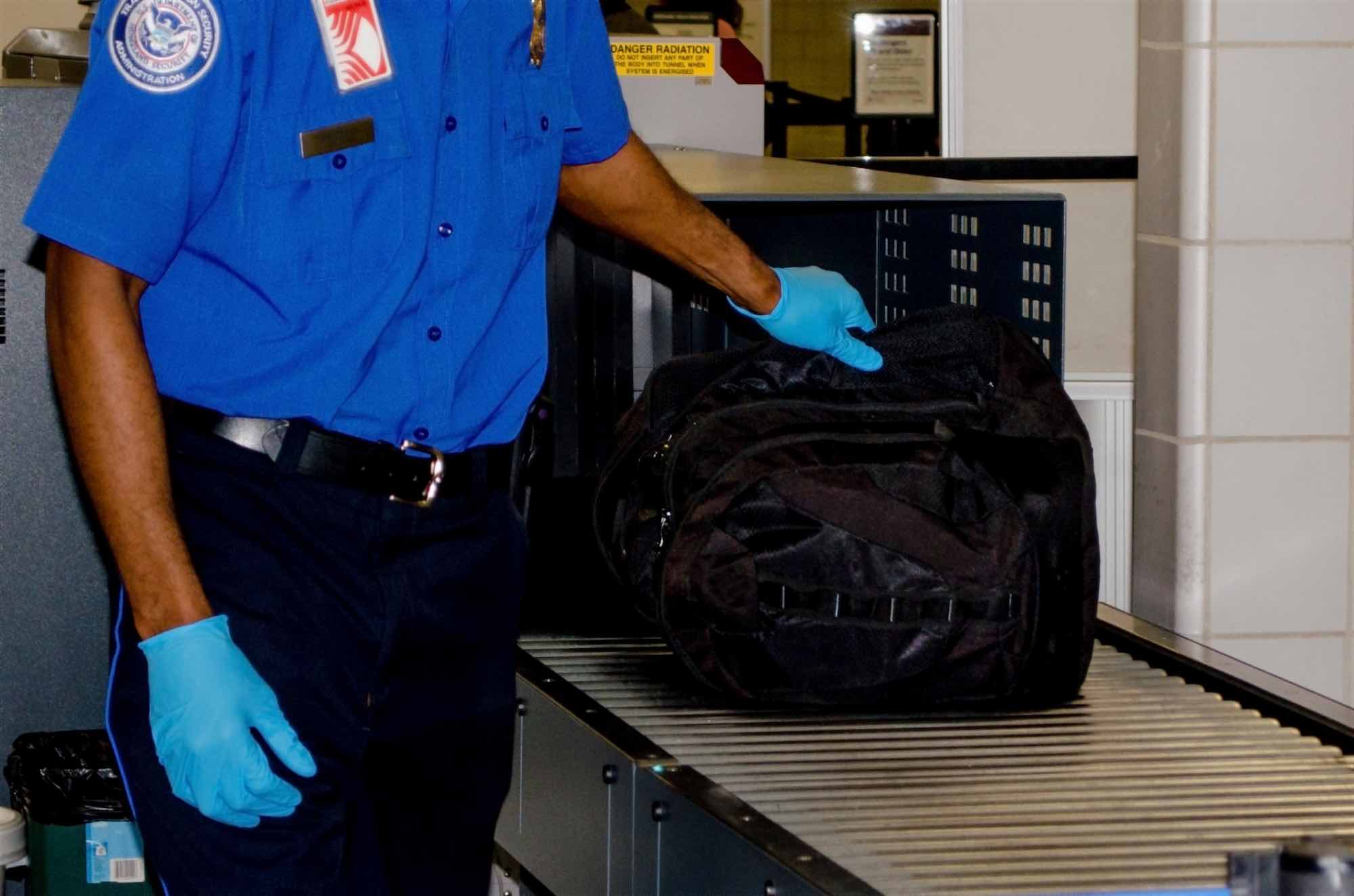 TSA agent putting bag through scanner on conveyor belt
