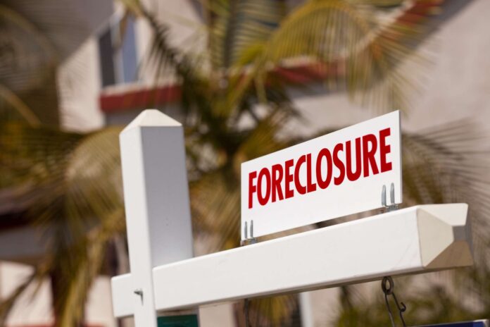 Foreclosure sign with palm trees and real estate home in background