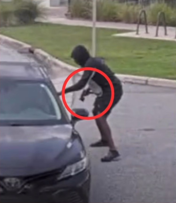 One of the suspects holding a gun while approaching the black sedan, moments before fleeing from the scene of the shooting.